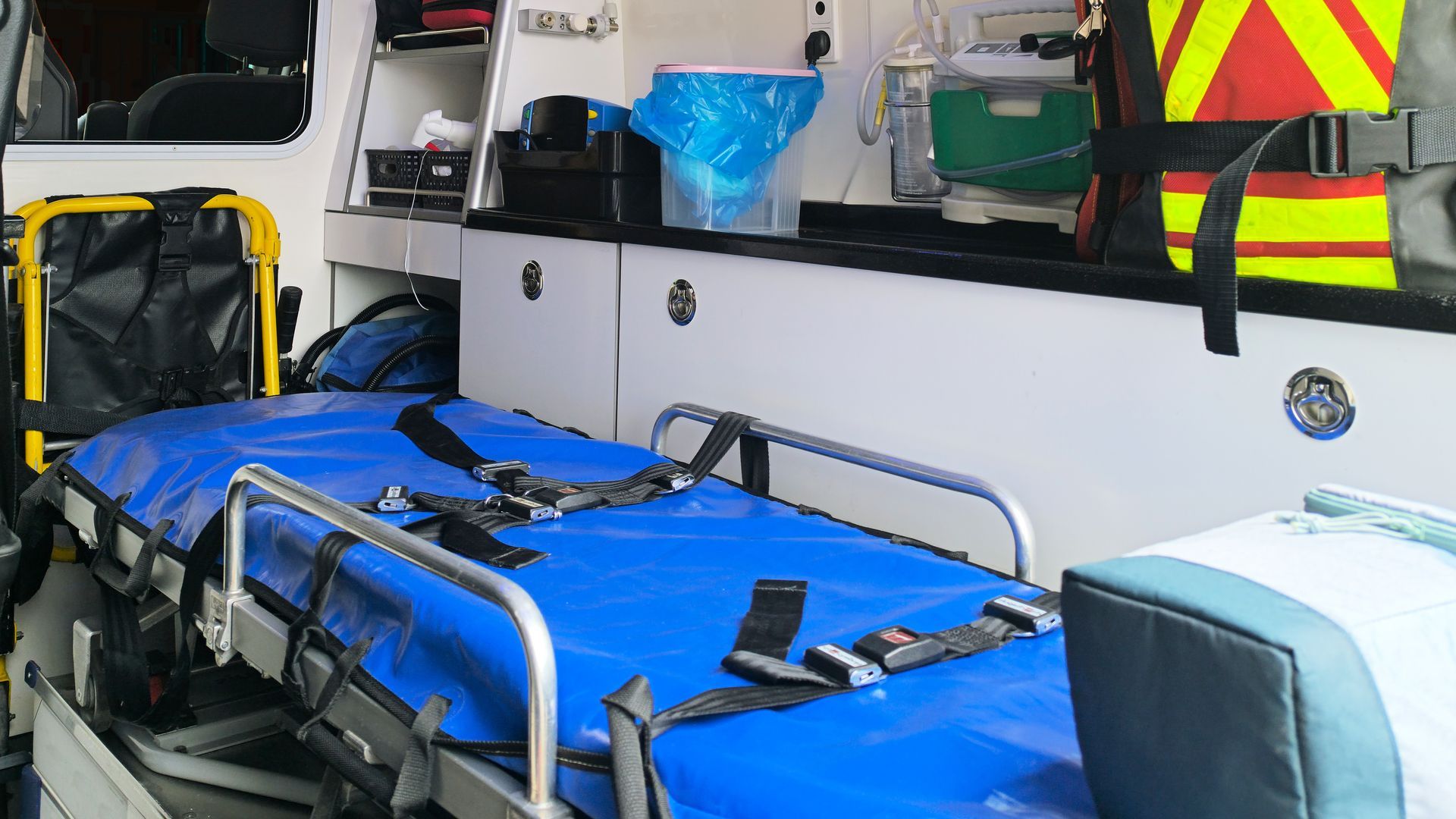 Intérieur d'une ambulance : civière bleue avec sangles de sécurité, armoires blanches, équipement.