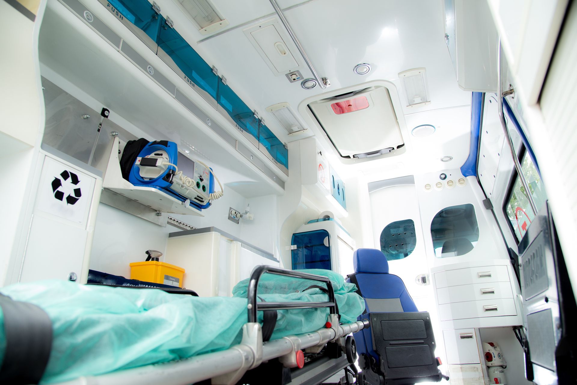 Intérieur d'une ambulance, vue arrière. Brancard avec un patient, matériel médical, bleu et blanc.