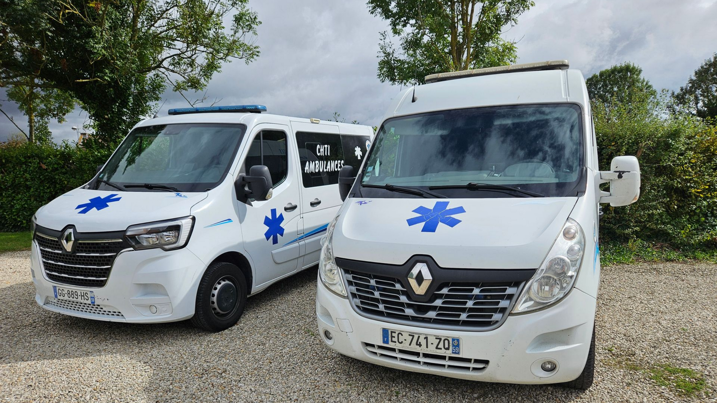 Deux ambulances blanches avec des étoiles bleues, stationnées à l'extérieur.