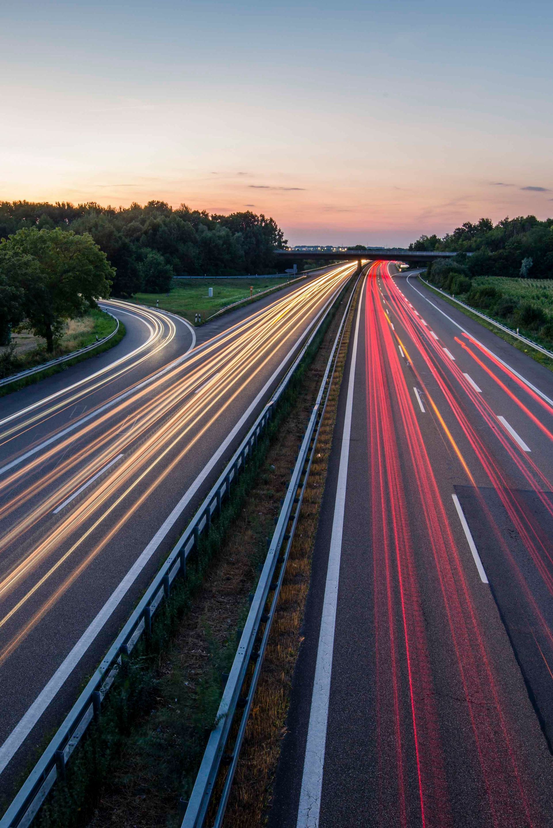 Autobahn mit Lichtstreifen von Autos im Sonnenuntergang.