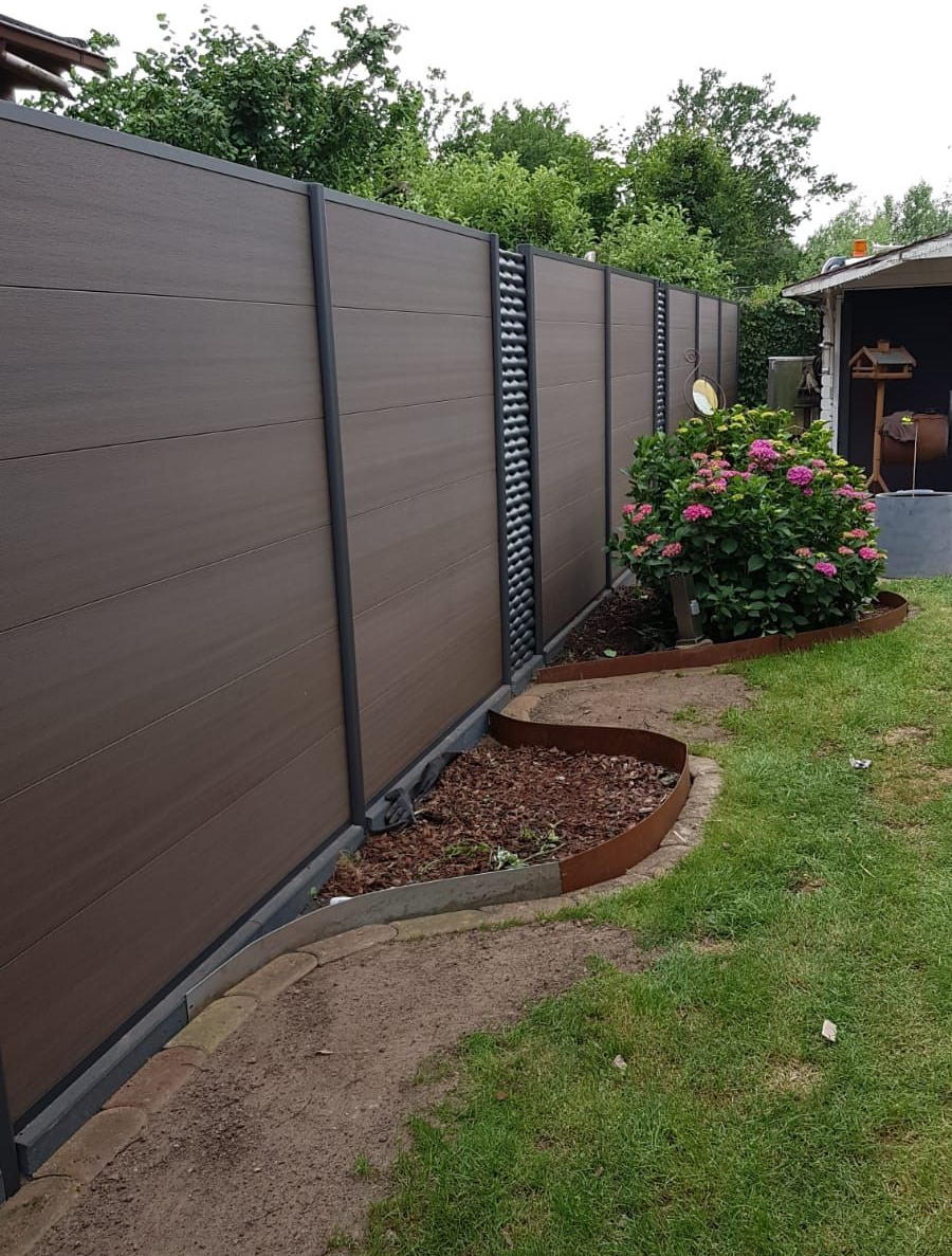 Brauner Sichtschutzzaun in einem Hinterhofgarten mit Blumenbeet und gemähtem Rasen.