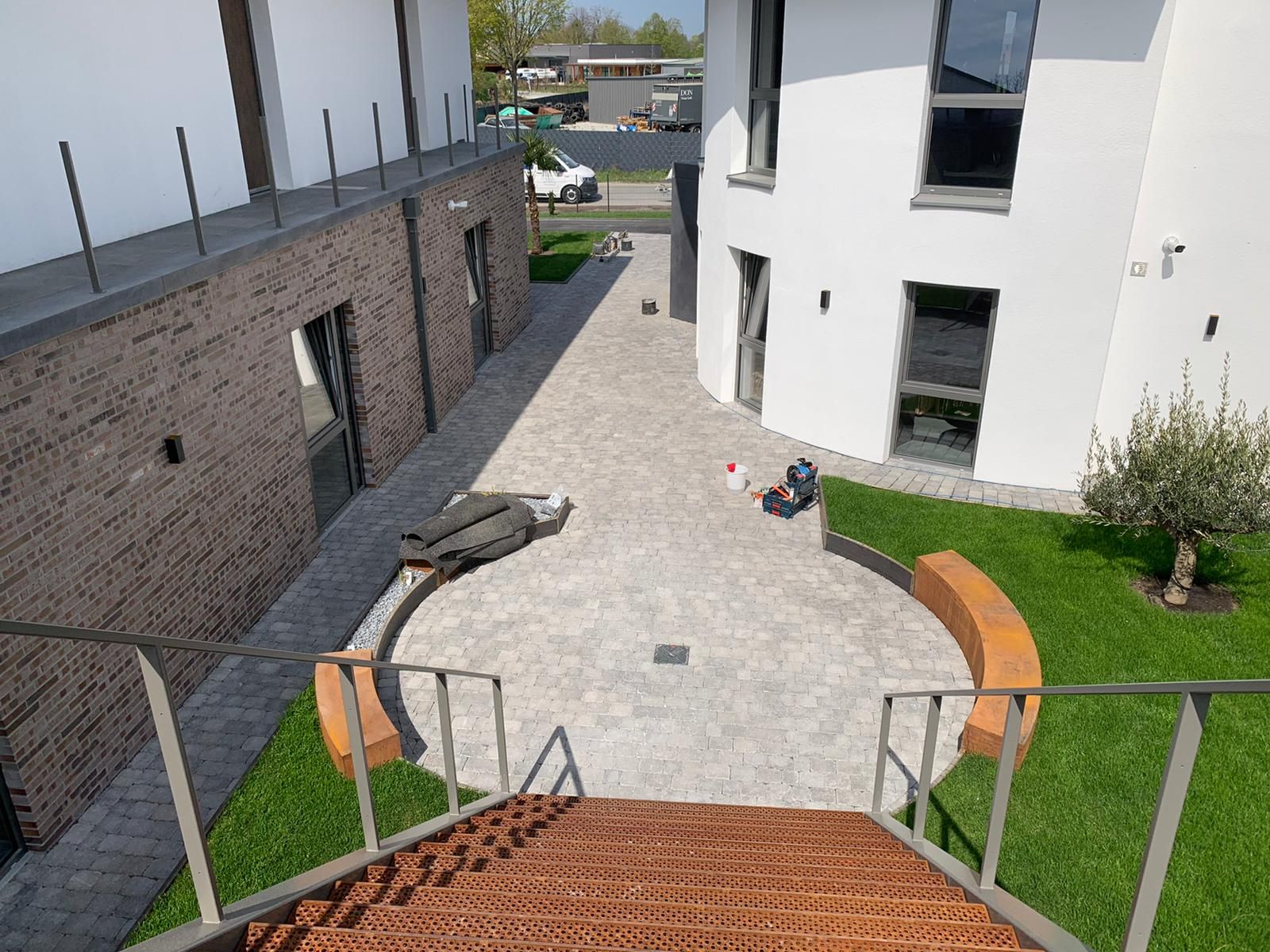 Innenhof mit Backstein- und weißen Gebäuden, Steinweg, grünem Rasen und geschwungenen Bänken.