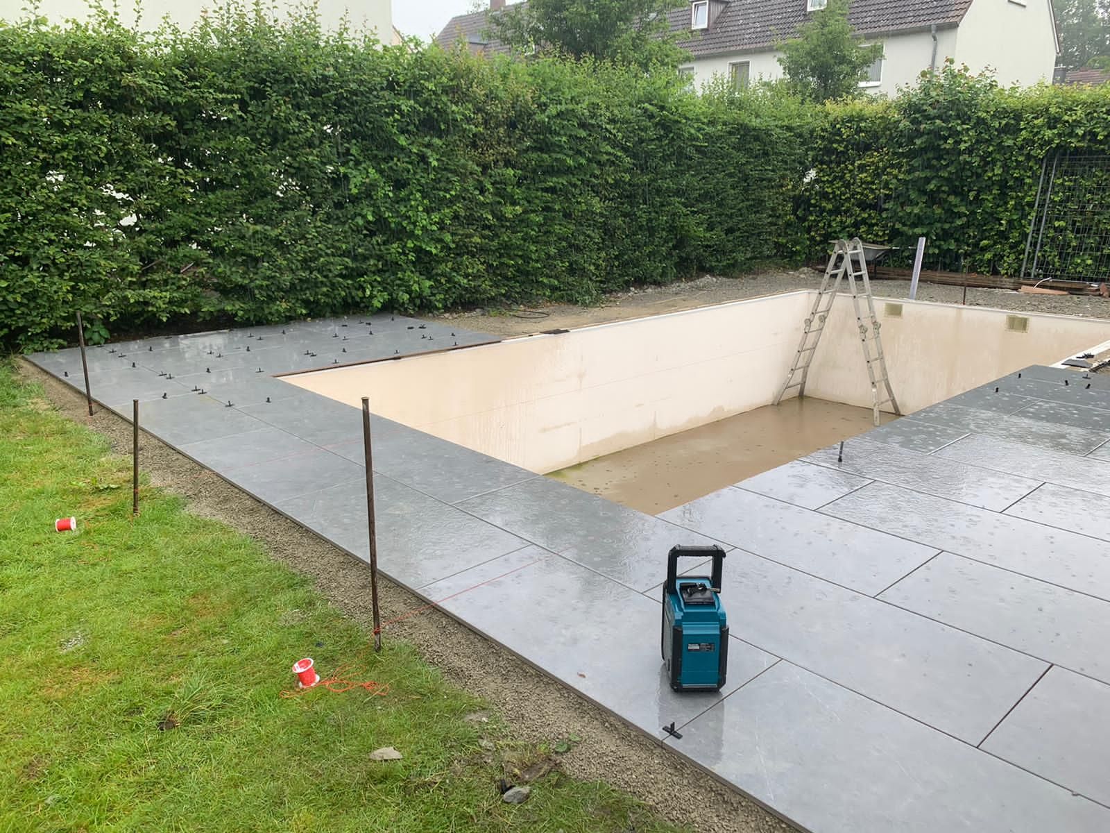 Baustelle mit einem teilweise errichteten Pool, umgeben von grauen Steinpflastersteinen.