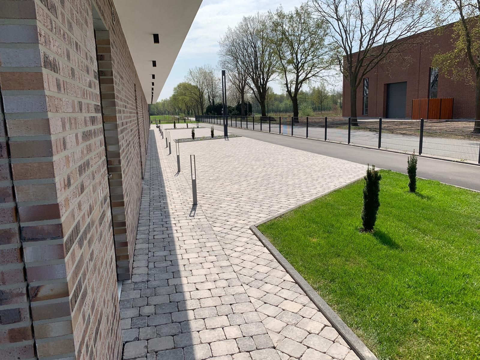 Fassade aus Backstein, Kopfsteinpflasterweg, Rasenfläche und Poller.