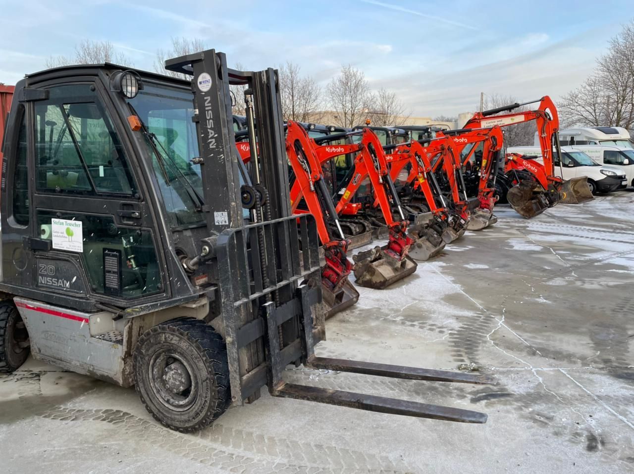 Eine Reihe von Baumaschinen, darunter ein Gabelstapler und Minibagger, parkt an einem verschneiten Tag im Freien.
