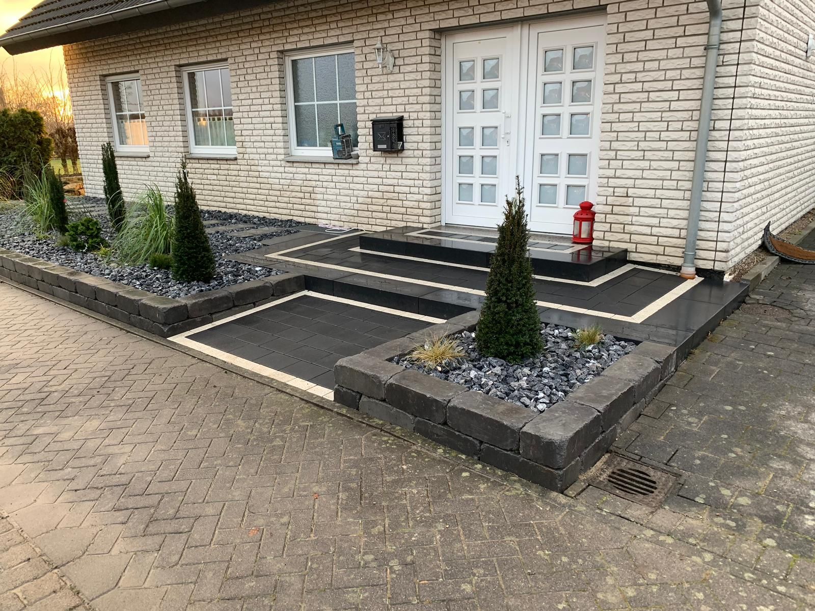 Die Fassade des Backsteinhauses ist mit dunkelgrauen Pflanzkübeln versehen, die mit Pflanzen und Steinen gefüllt sind.