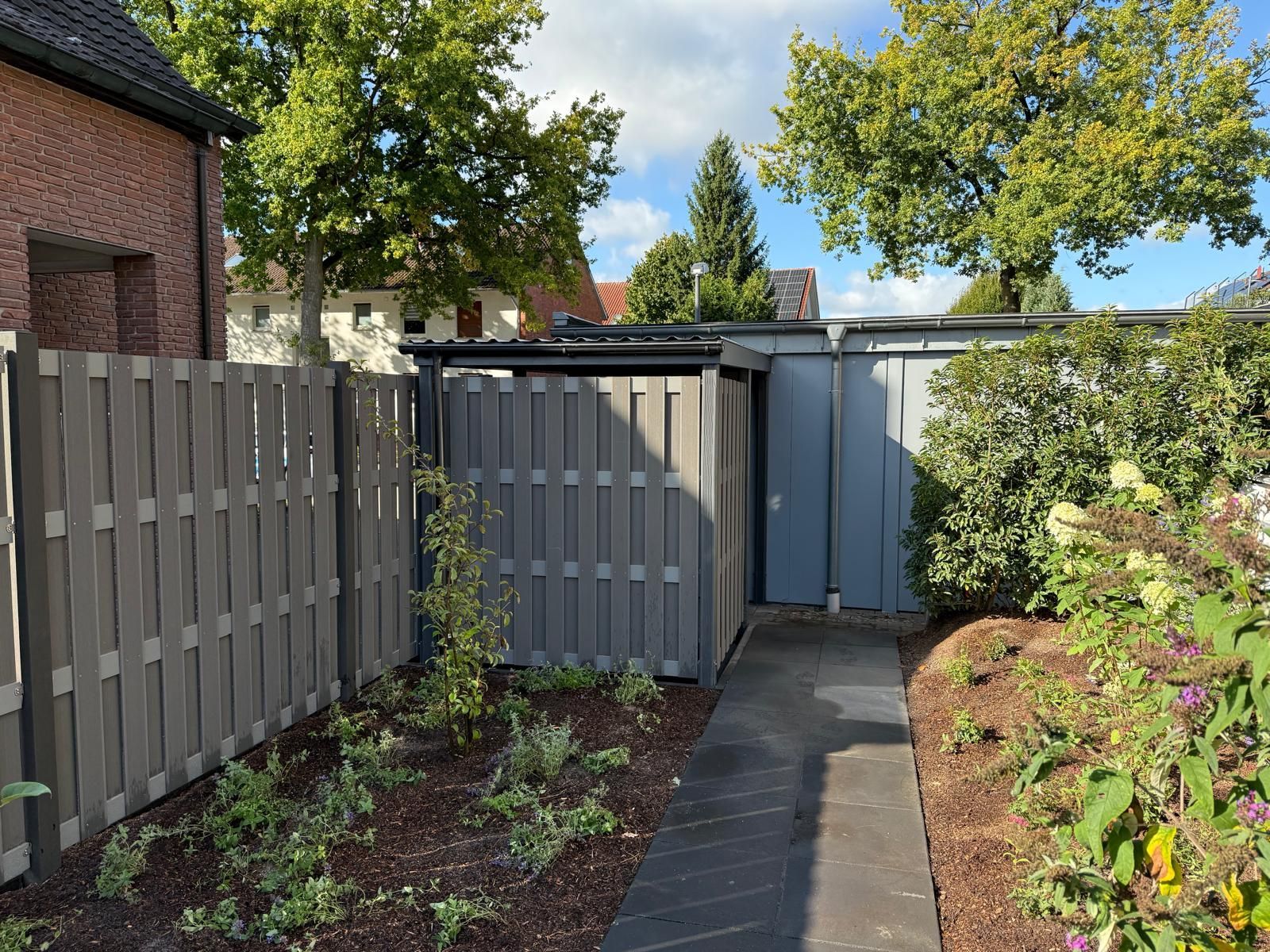 Grauer Sichtschutzzaun und Gartenhaus mit einem Steinweg in einem Garten.