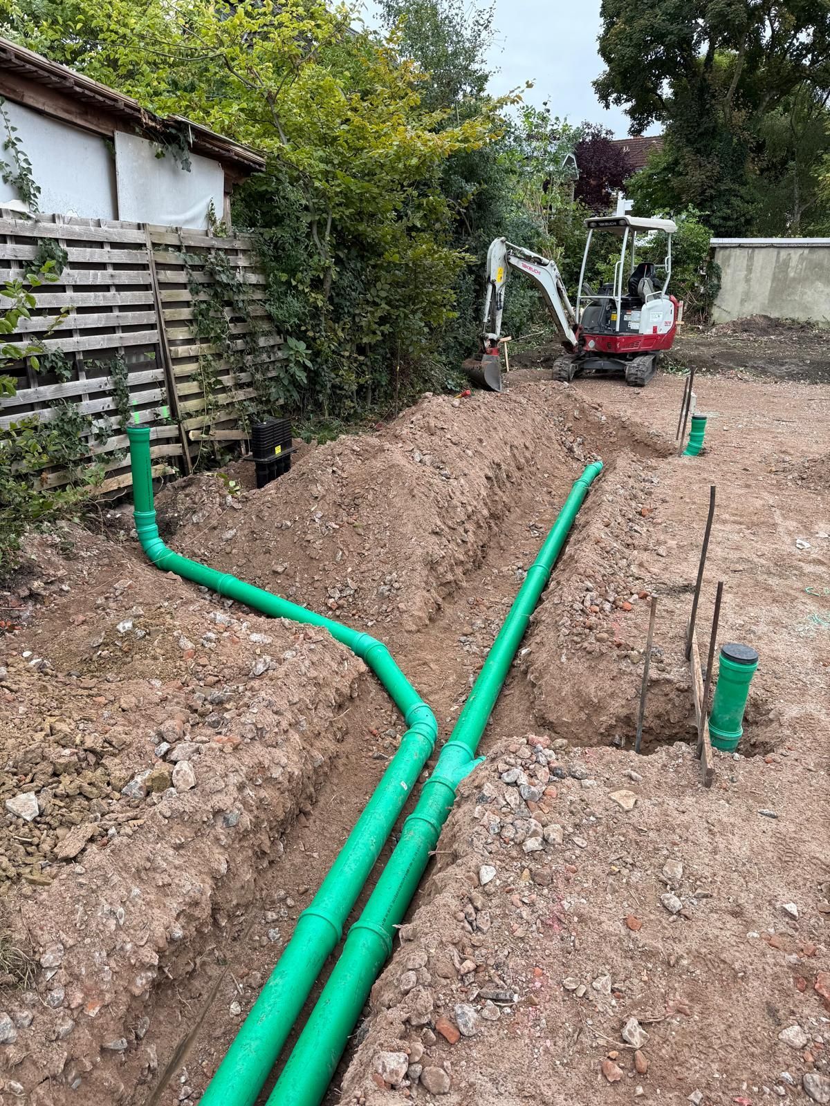 Grüne Rohre in Gräben verlegt, Baustelle mit Bagger im Hintergrund.