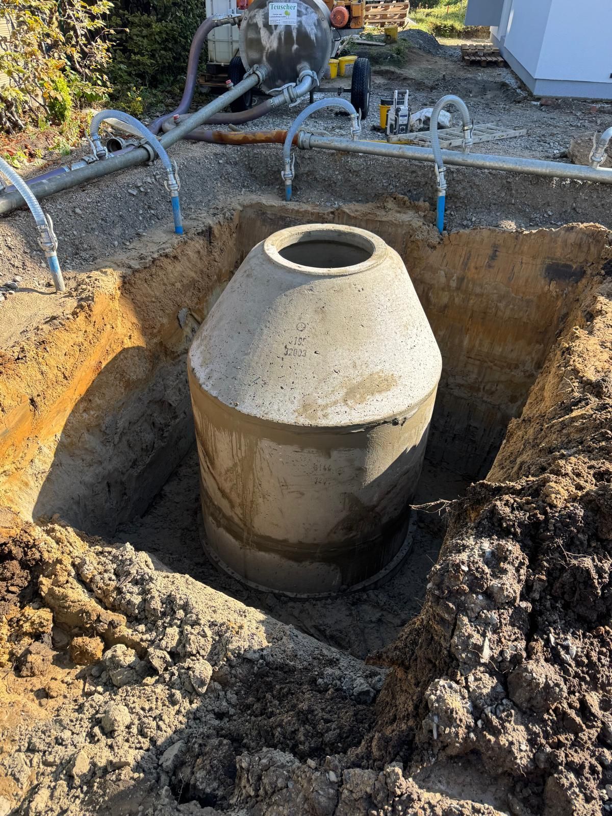 Klärgrube aus Beton in einer ausgehobenen Grube, an deren Oberseite Schläuche angeschlossen sind.