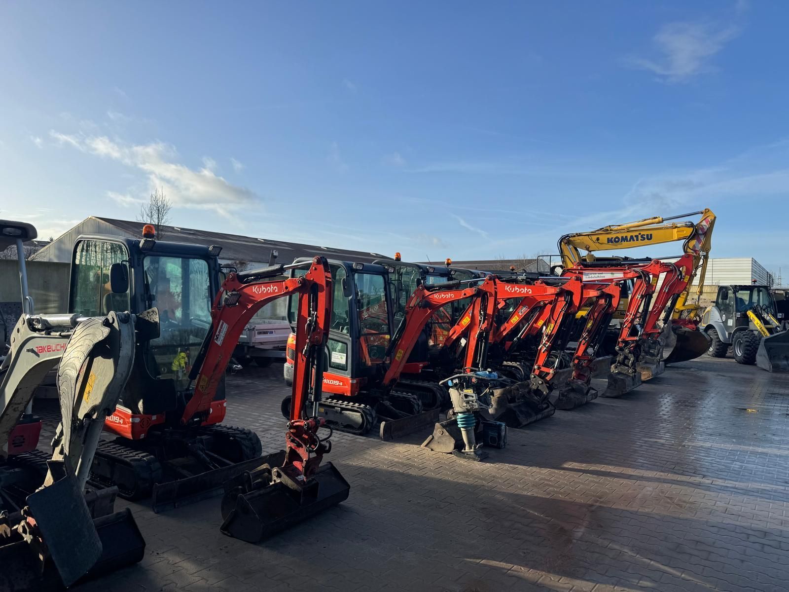 Eine Reihe roter und gelber Bagger parkt an einem sonnigen Tag draußen.
