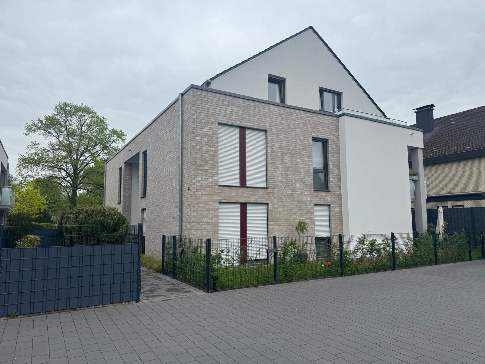 Modernes Backsteinhaus mit weißen Fassaden, dunklen Fensterrahmen und schrägem Dach unter bewölktem Himmel.