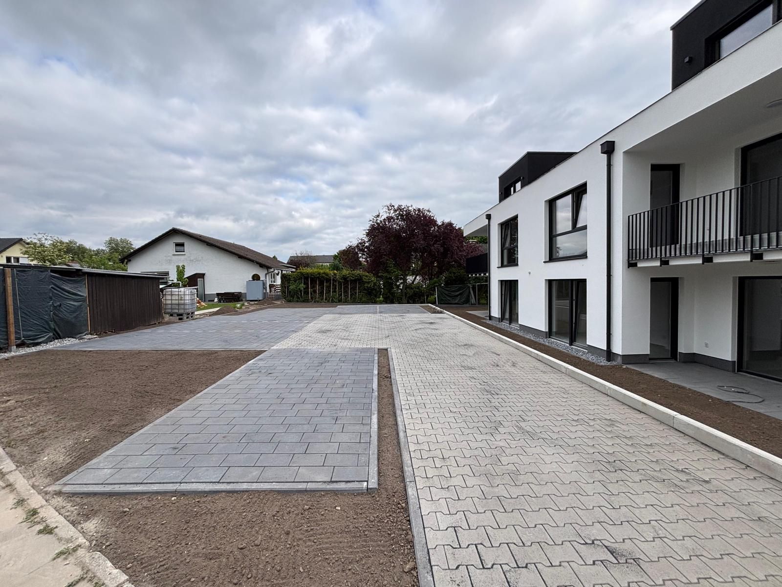 Ein leerer Parkplatz neben einem modernen Gebäude, gepflastert mit grauen Pflastersteinen, an einem bewölkten Tag.