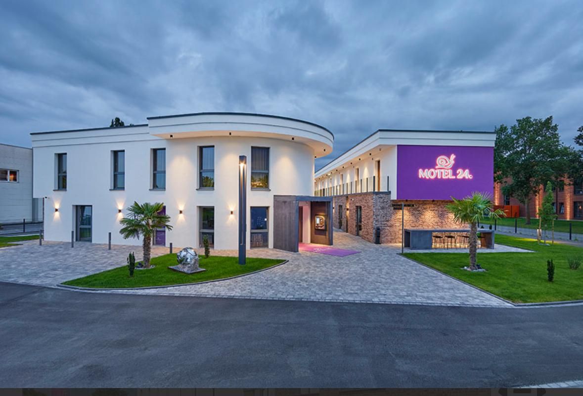 Das Hotel 24 mit seinen weißen Wänden, dem geschwungenen Abschnitt und der Steinfassade, die von Außenleuchten erhellt wird, vor einem bewölkten Himmel.