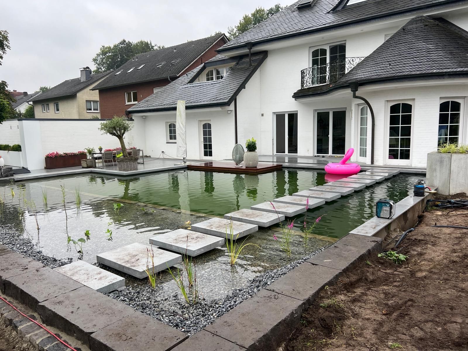 Hinterhof mit großem Teich, Steintreppe und einem weißen Haus mit dunklem Dach.