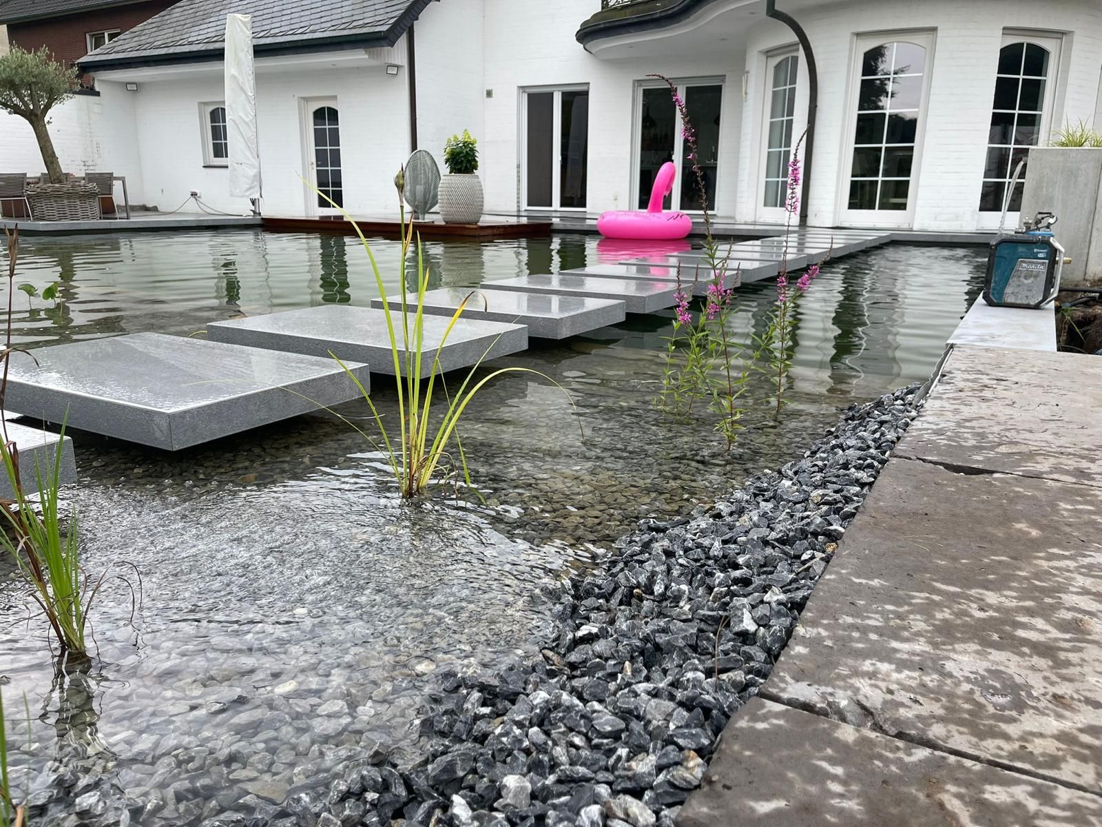 Wasserspiel mit Trittsteinen, fließendem Wasser und einem weißen Haus im Hintergrund.