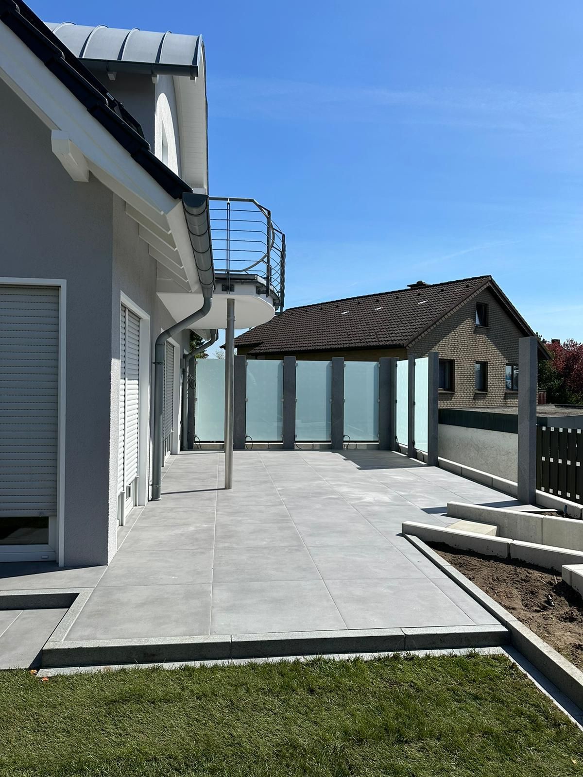 Außenansicht eines modernen Hauses mit Terrasse, Pergola und klarem Himmel.
