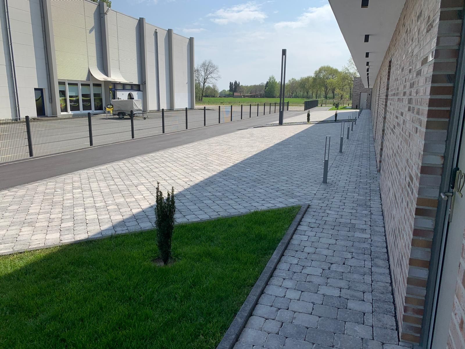 Kopfsteinpflasterweg neben einem Gebäude mit Rasenfläche und modernem Architekturstil.