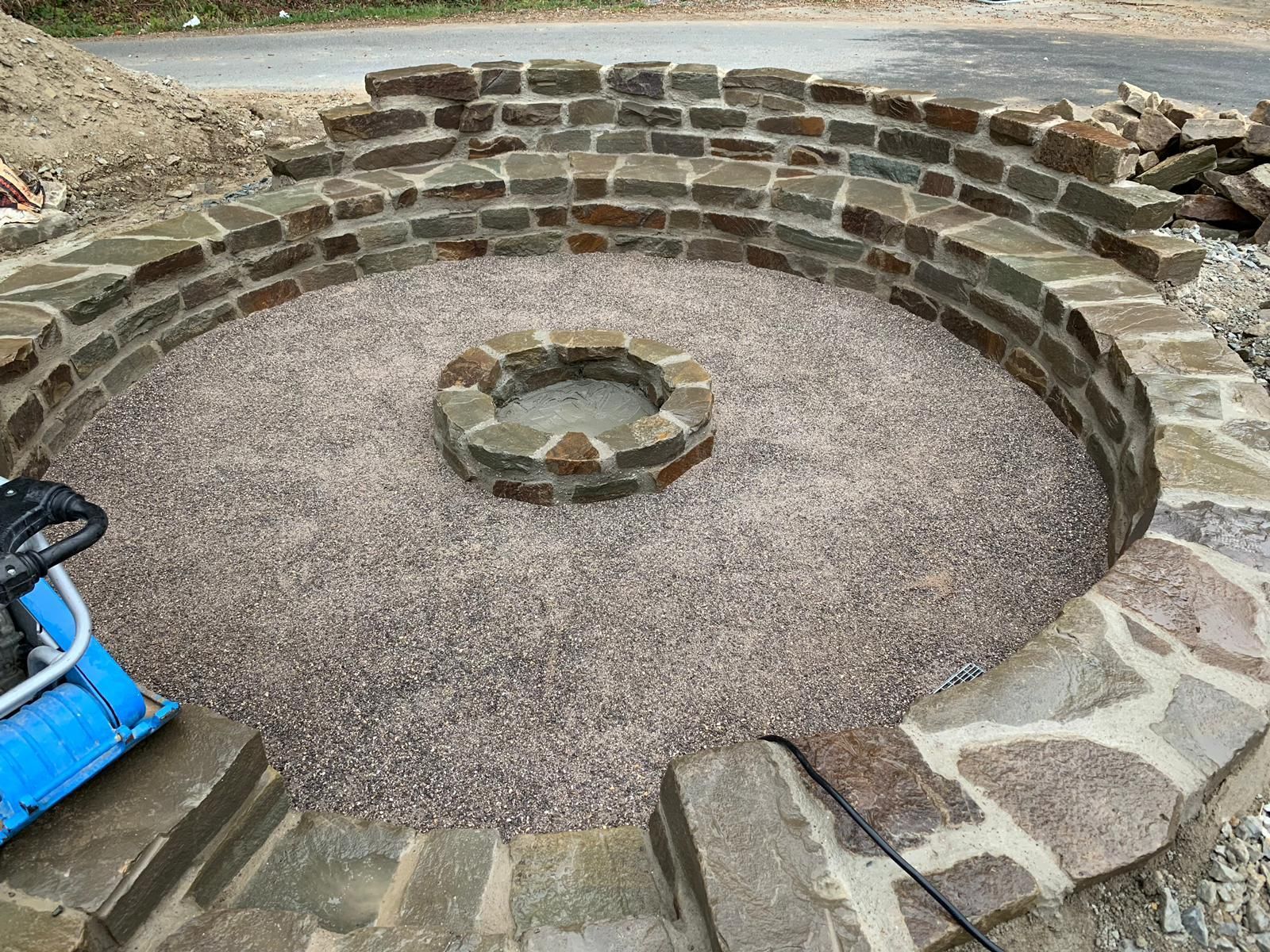Im Bau befindliche runde Feuerstelle aus Stein mit Kiessockel und Sitzgelegenheiten aus Stein.
