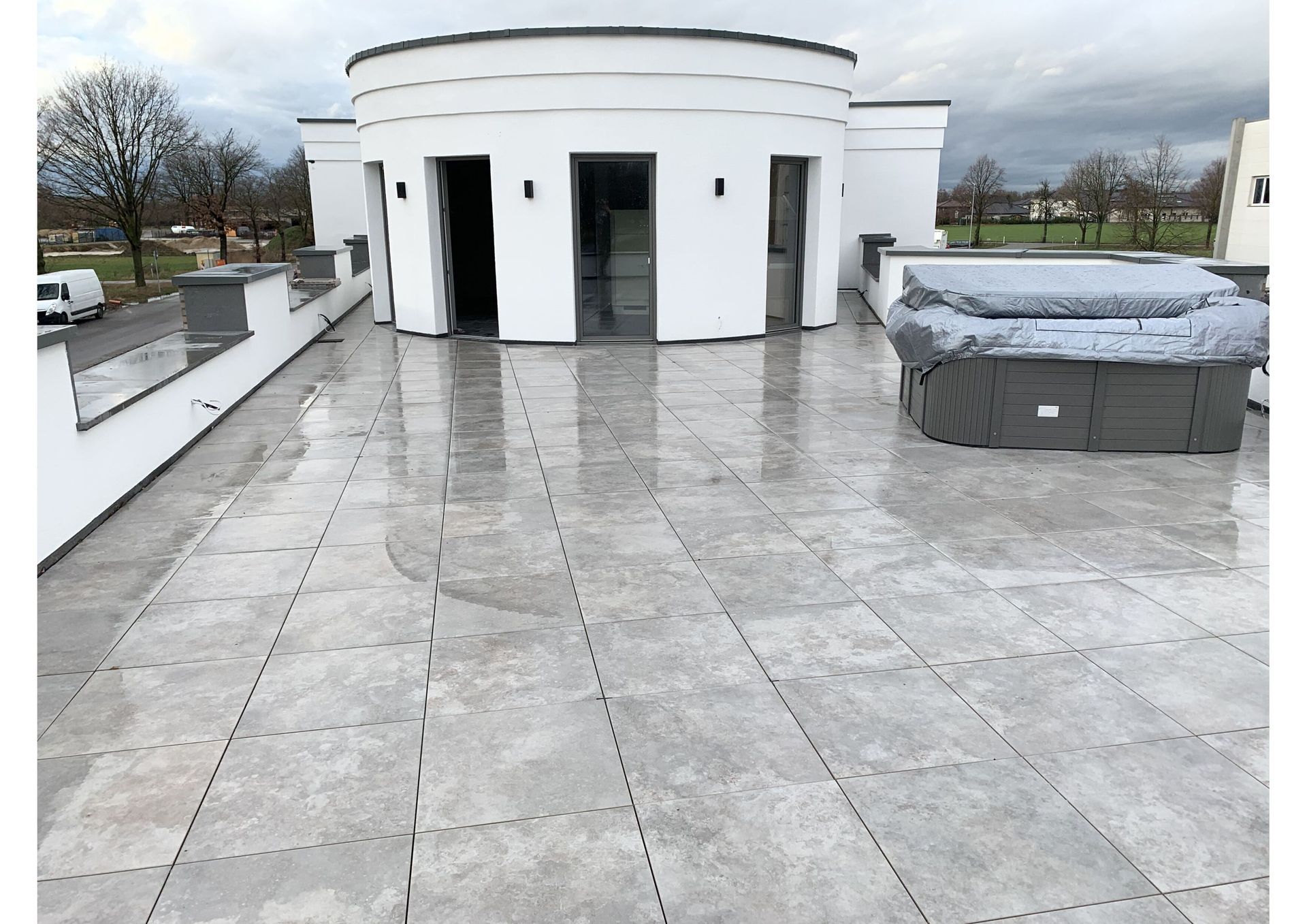 Graues Ziegeldach mit weißem zylindrischem Aufbau und überdachtem Whirlpool. Bewölkter Himmel.