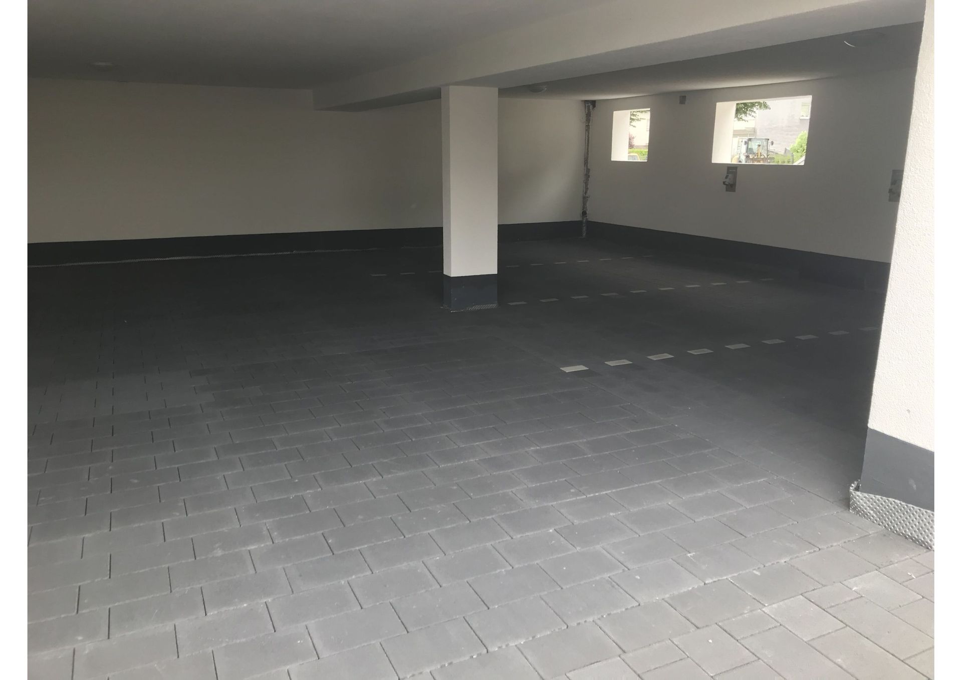Parkhaus mit grauem Ziegelboden und weißen Wänden.