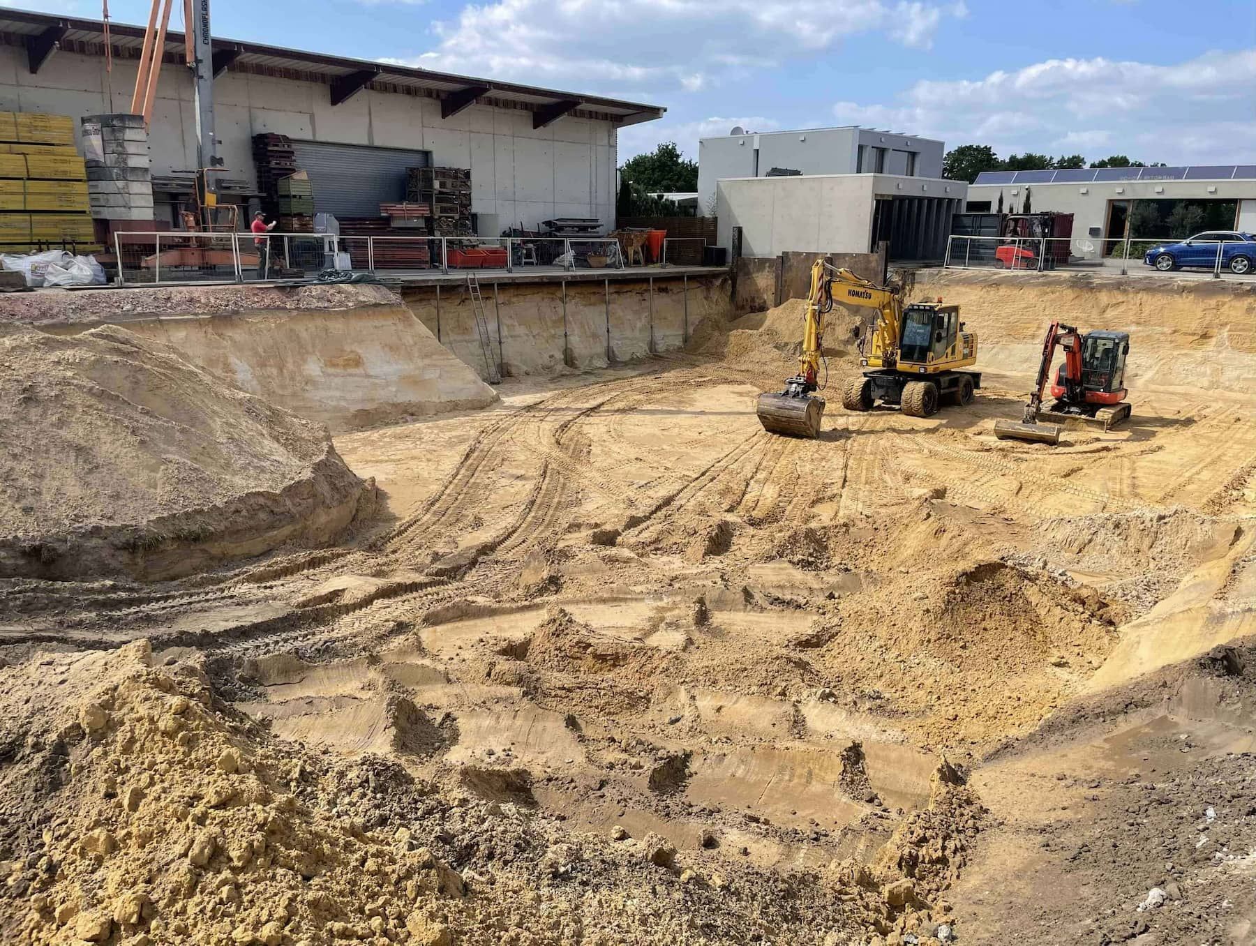Baustelle mit zwei Baggern in einer großen Baugrube in der Nähe eines Gebäudes.