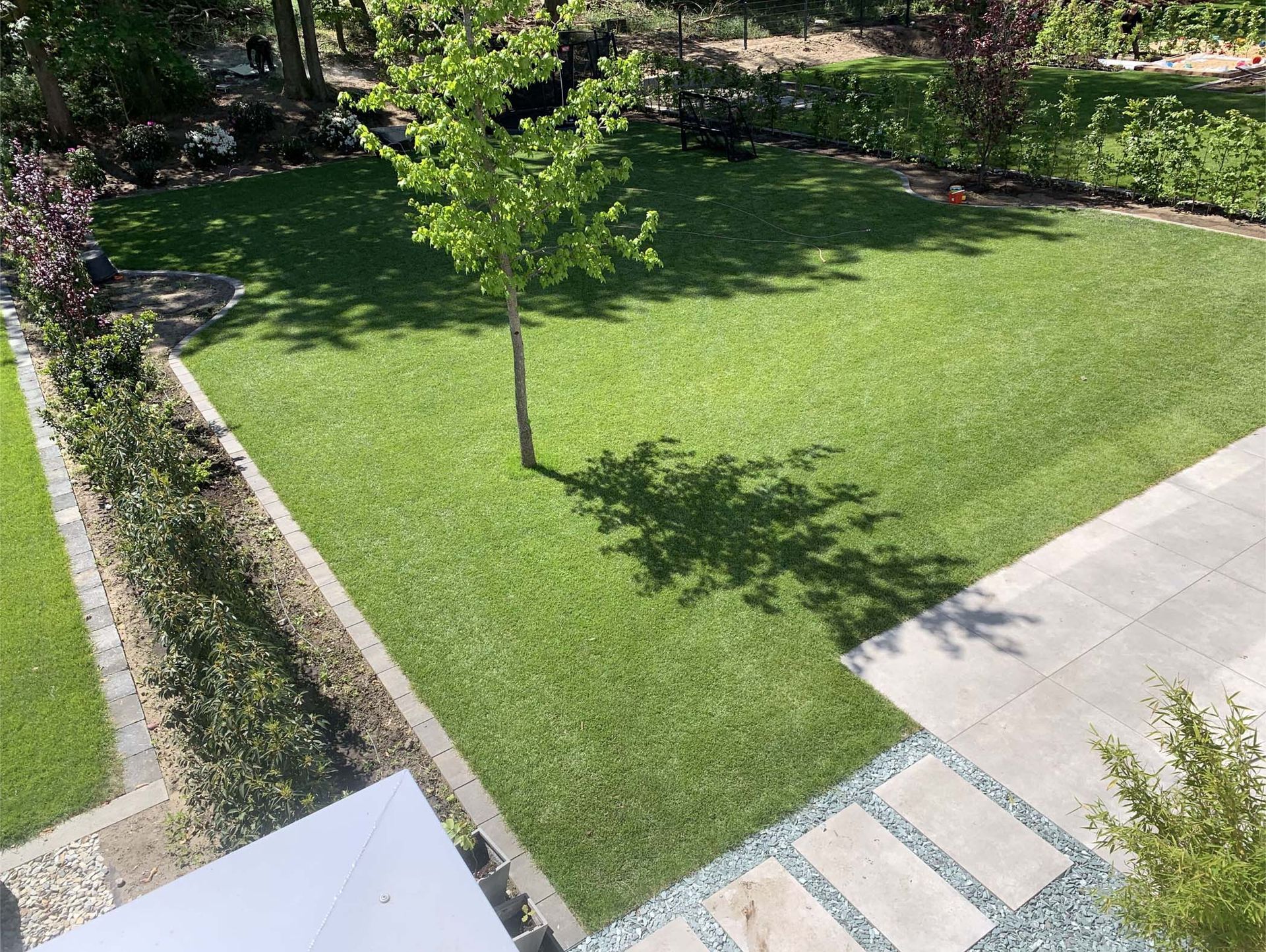 Ein üppiger grüner Rasen mit einem jungen Baum, umgeben von akkurat geschnittenen Hecken und Steinwegen.