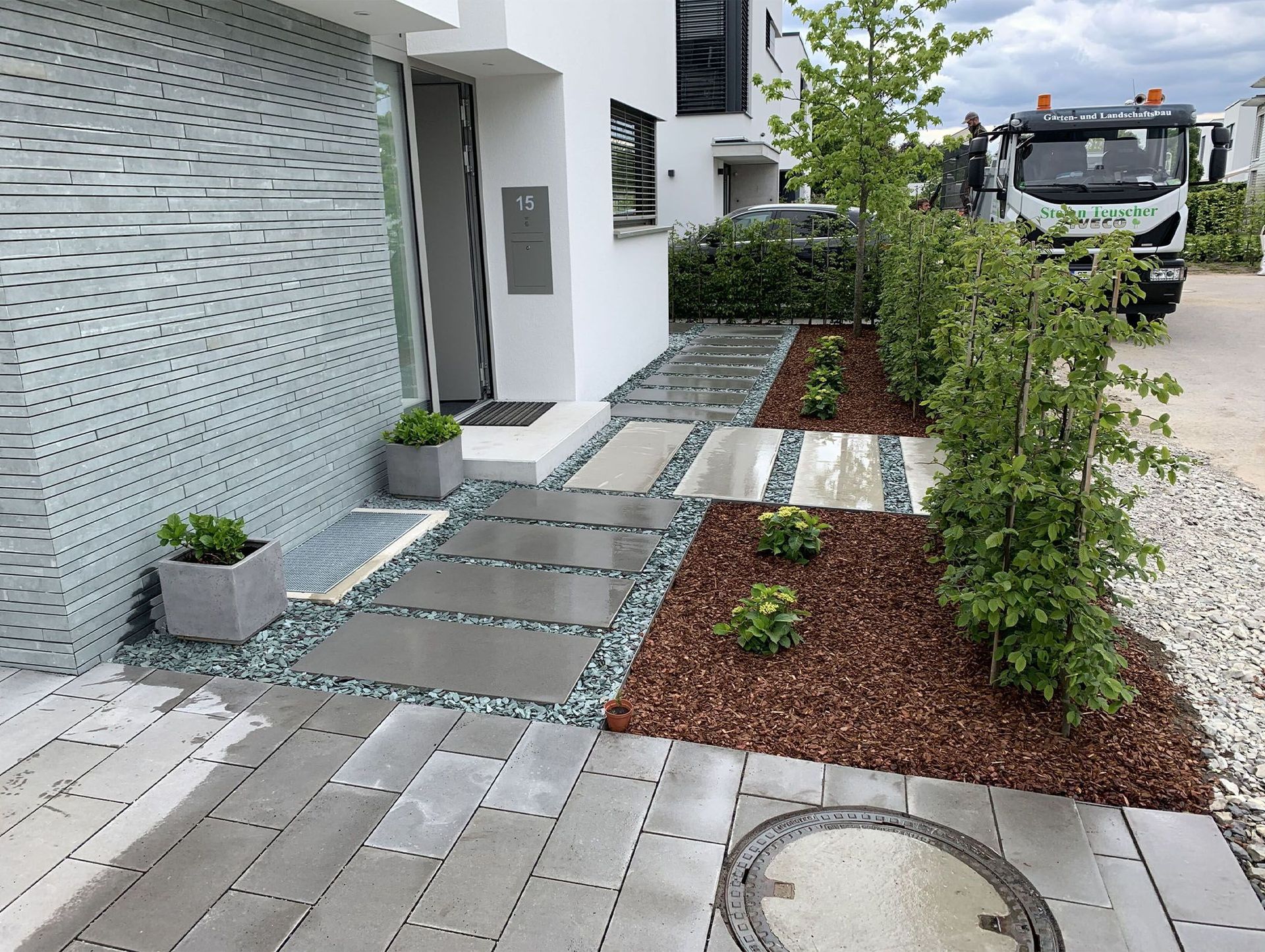 Moderner Hauseingang mit Steinweg, Gartengestaltung und einem Lastwagen.