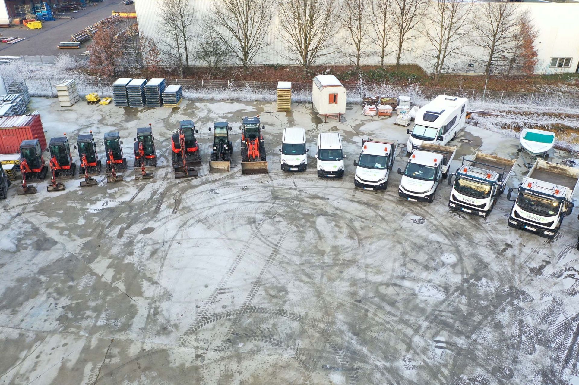 Luftaufnahme eines verschneiten Grundstücks mit einer Reihe von Baufahrzeugen und Lieferwagen.