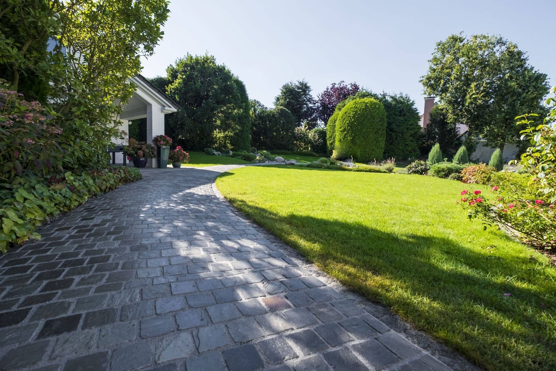 Ein Steinweg schlängelt sich durch einen üppig grünen Rasen und führt zu einem weißen Haus, im Hintergrund sind Bäume zu sehen.