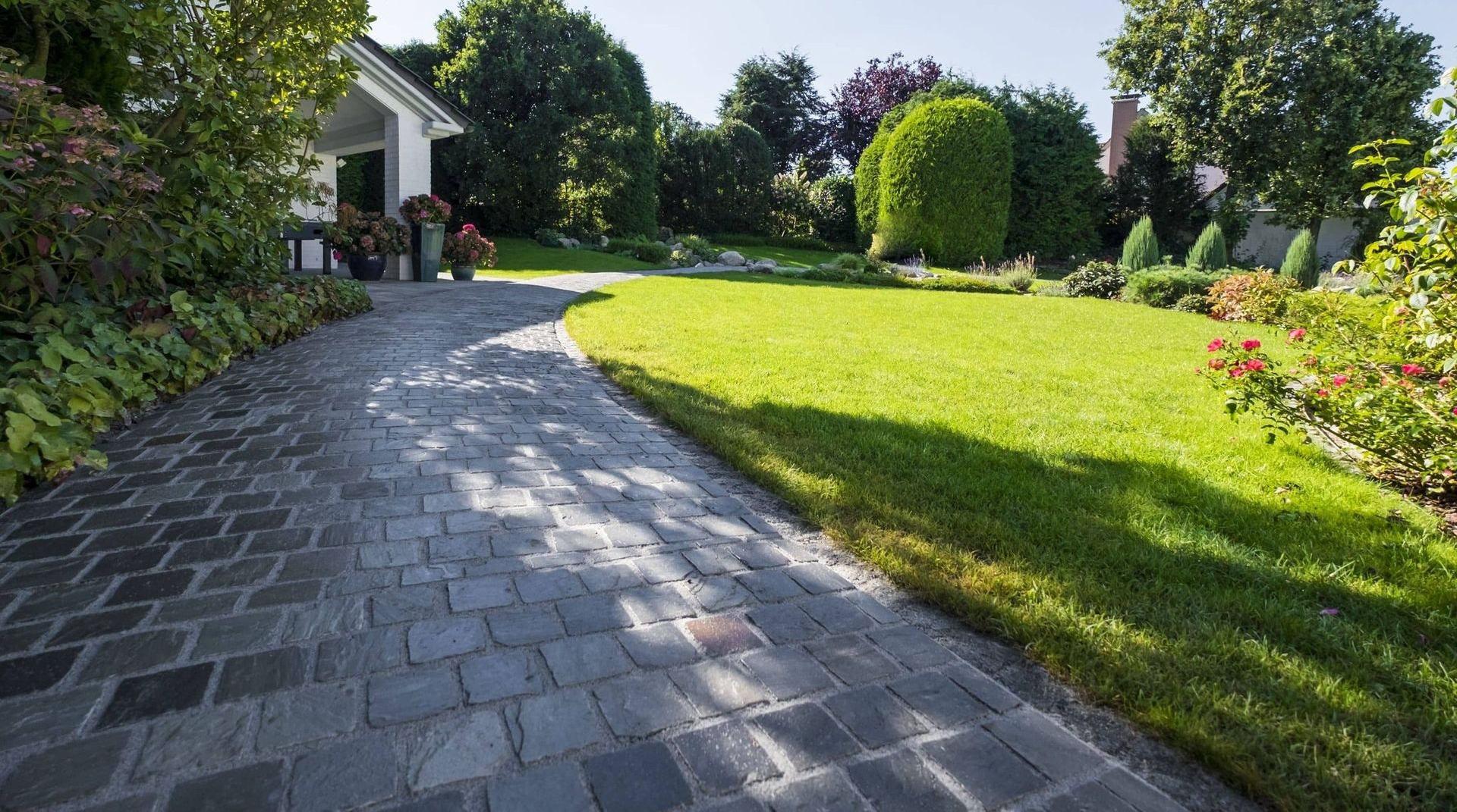 Eine mit Kopfsteinpflaster belegte Auffahrt schlängelt sich durch einen üppig grünen Rasen zu einem weißen Haus.