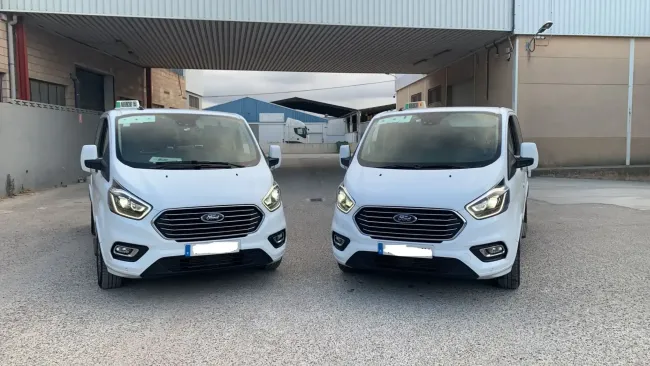 Dos furgonetas blancas están estacionadas frente a un edificio.