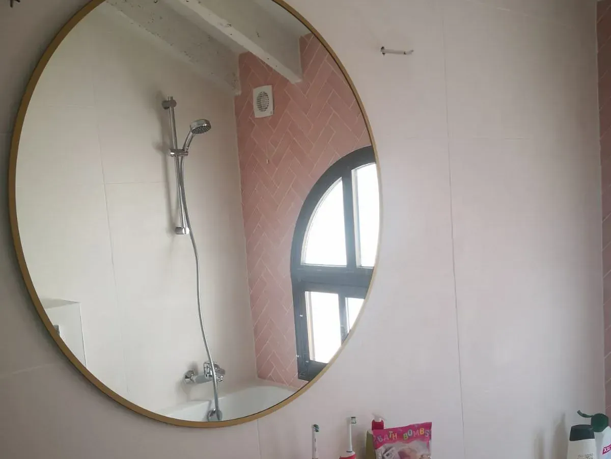 Un baño con un espejo redondo y una ventana.