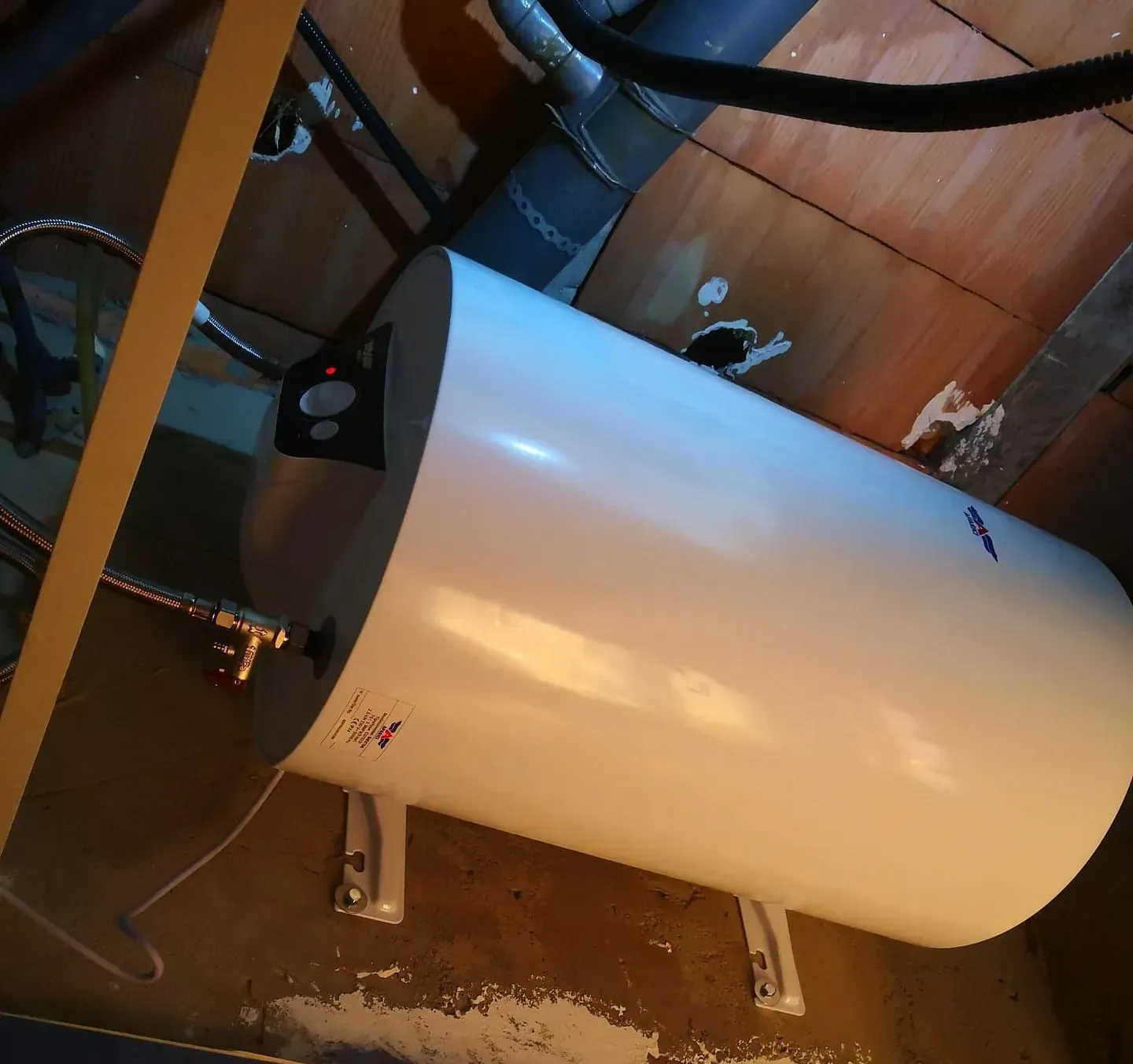 Un calentador de agua blanco está sobre un piso de madera.