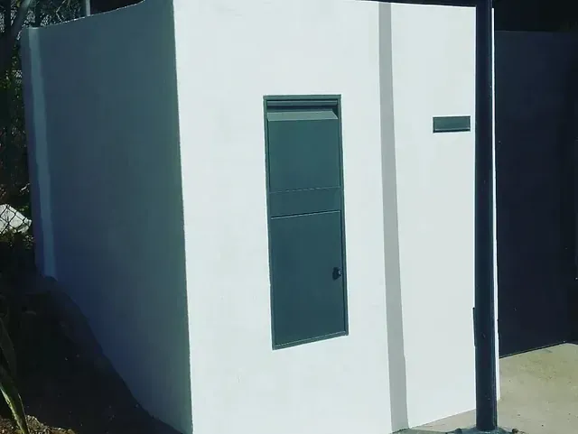 Un edificio blanco con una puerta negra y un buzón en el costado.