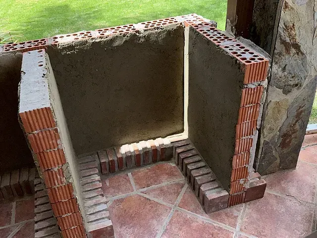 Se está construyendo una chimenea de ladrillo sobre un suelo de baldosas.