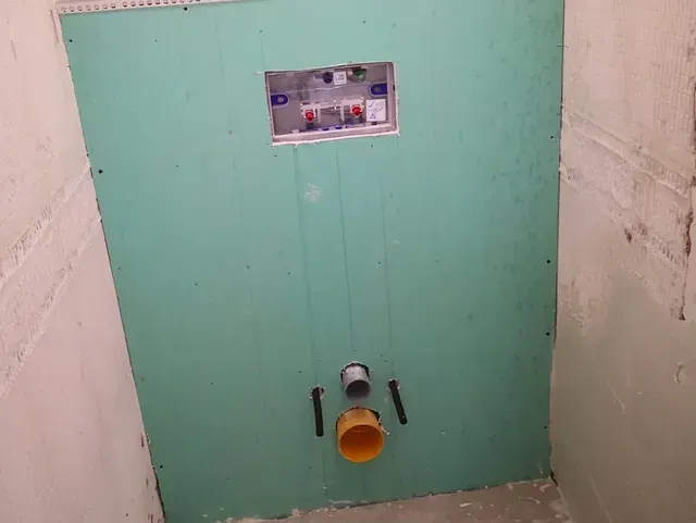 Se está construyendo un inodoro en un baño con una pared verde.