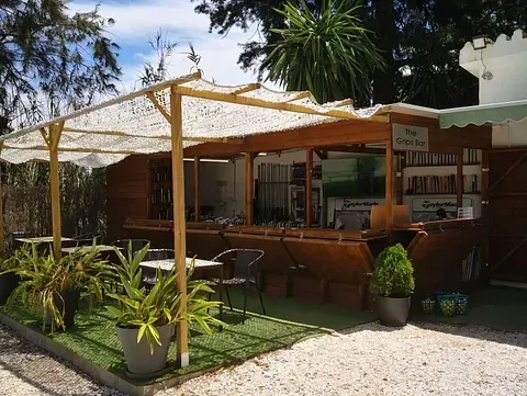 Un restaurante con mesas, sillas, sombrillas y plantas delante.