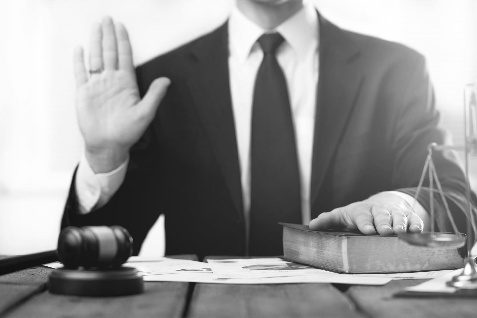 Un hombre con traje y corbata está sentado en una mesa con la mano levantada.