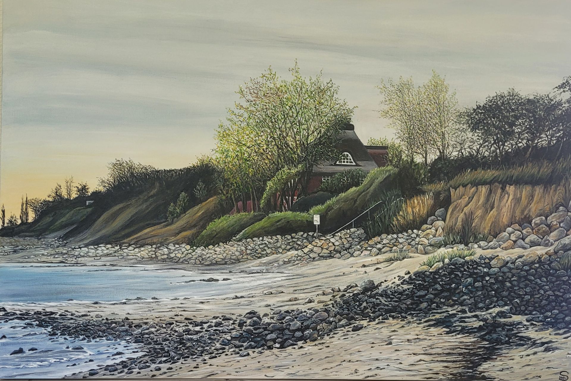 Küstenlandschaft mit einem Haus auf einer Klippe mit Blick auf einen felsigen Strand und das Meer unter einem bewölkten Himmel.