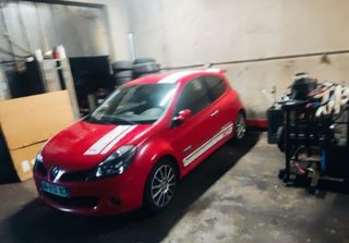 Une voiture rouge à hayon est garée dans un garage à côté de matériel et de cartons empilés.