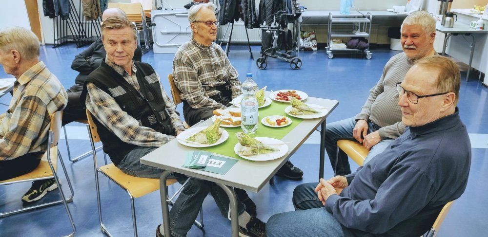 Neljä miestä istuu pöydän ympärillä ruokalautasten kanssa.