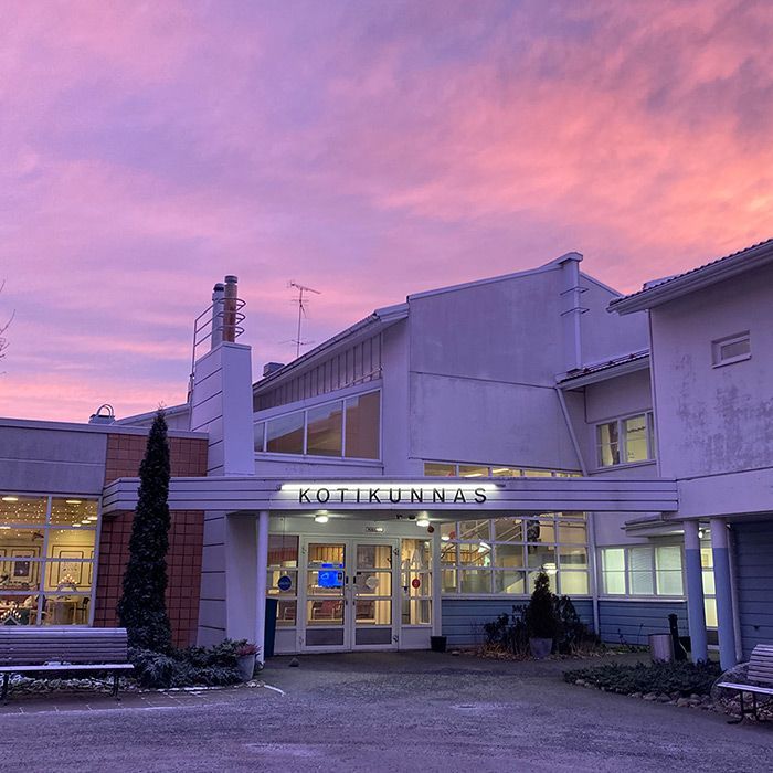 Kotikunnaan sisäänkäynti vaaleanpunaista ja violettia auringonlaskua vasten.