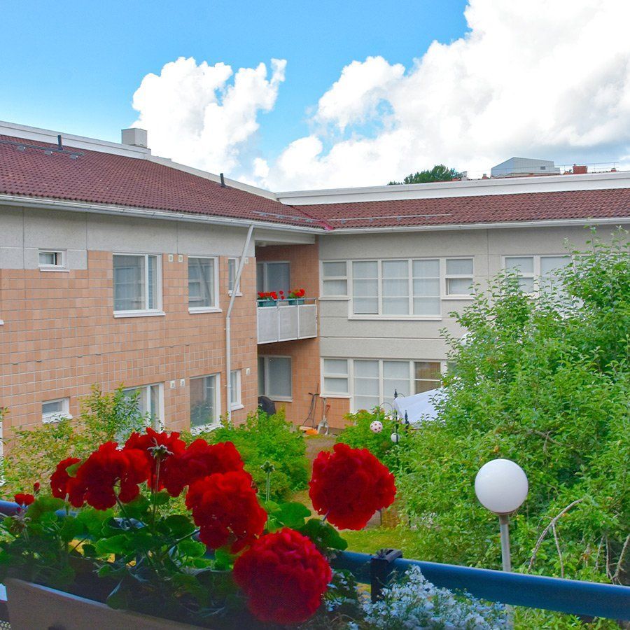 Kerrostalon ulkokuva, jossa etualalla punaisia ​​kukkia.