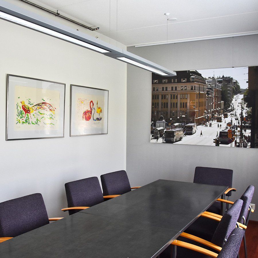 Kokoushuone, jossa on pitkä tumma pöytä, violetit tuolit ja kehystettyjä taideteoksia. Seinällä suuri Turun katukuva.