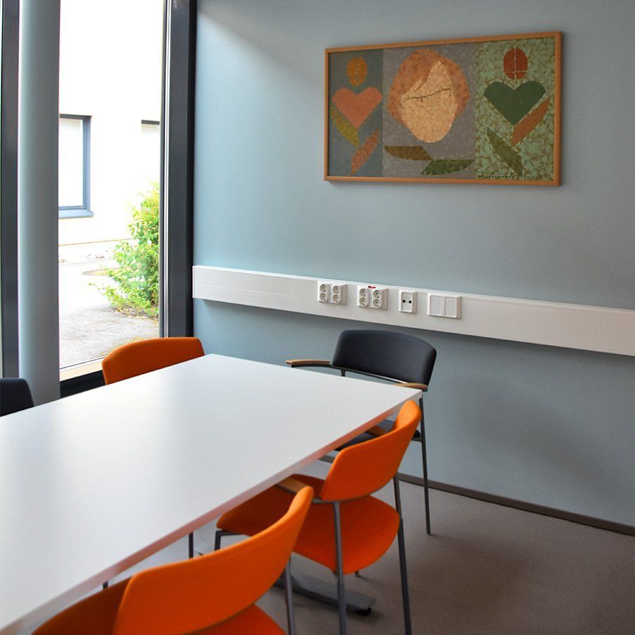 Kokoushuone, jossa on valkoinen pöytä ja oranssit tuolit, taidetta seinällä ja suuri ikkuna.
