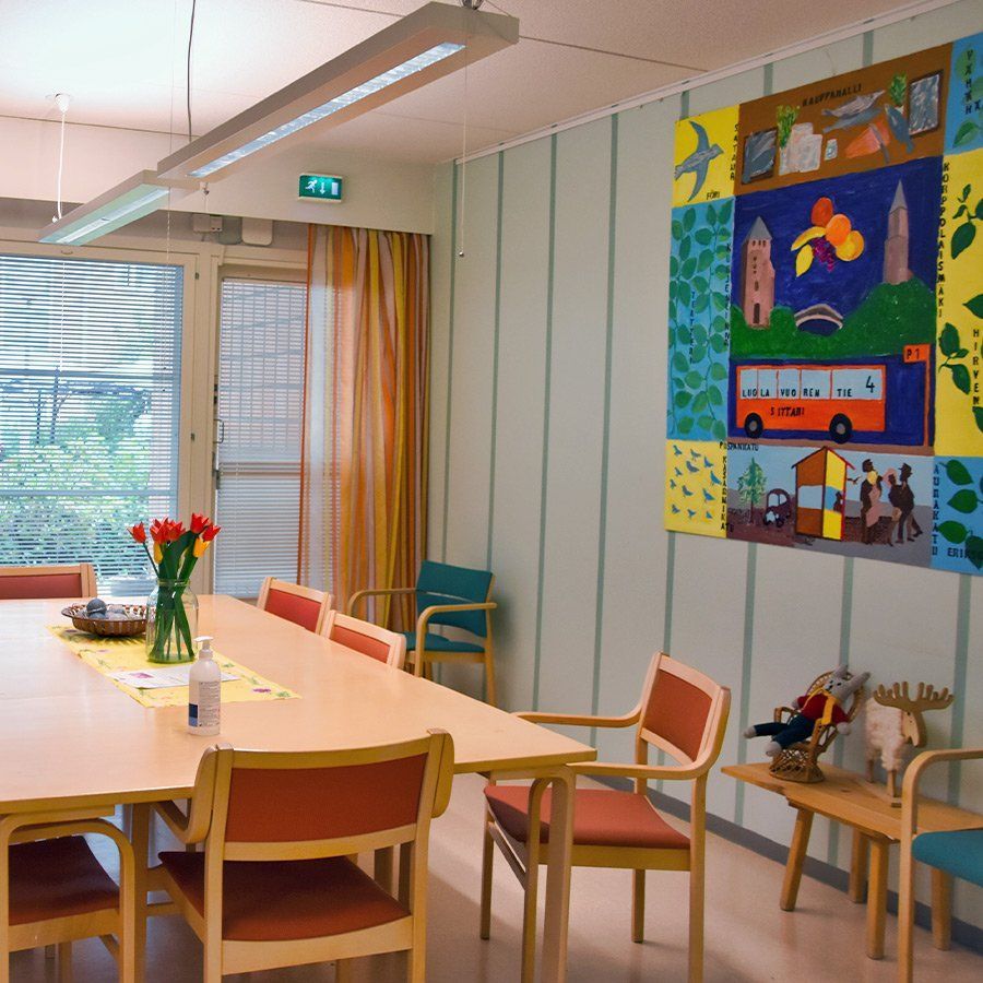 Valoisa ruokasali, jossa on pitkä puinen pöytä ja värikkäitä taideteoksia seinillä.