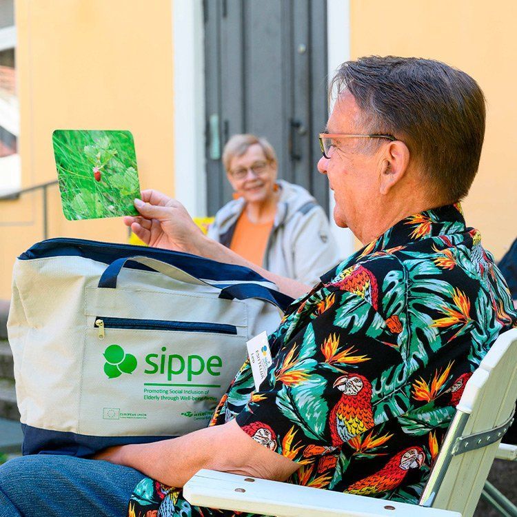 Tuolissa istuva mies pitelee leppäkerttua esittävää korttia laukku sylissään.