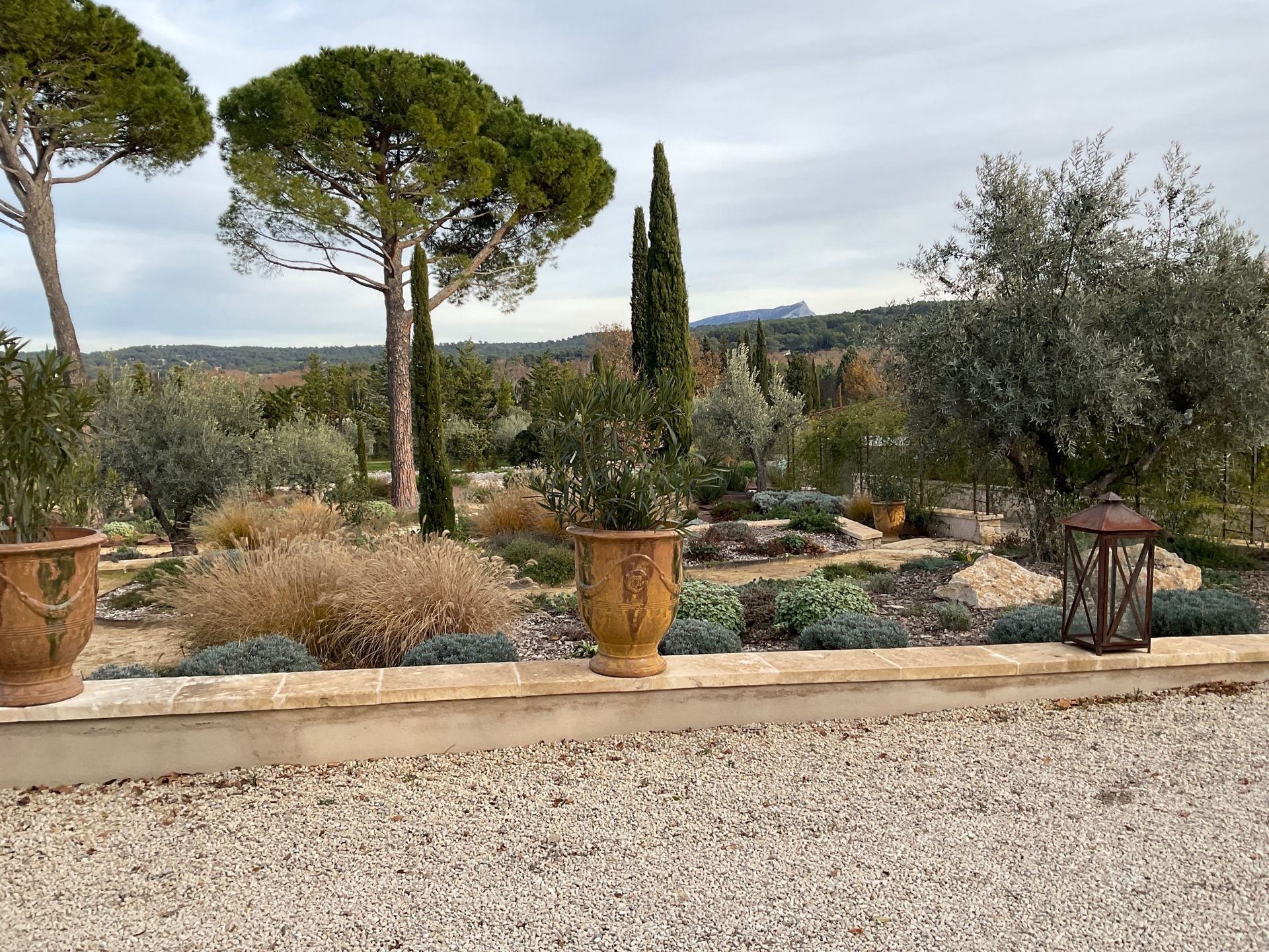 Une allée de gravier avec des plantes en pot et des arbres en arrière-plan.