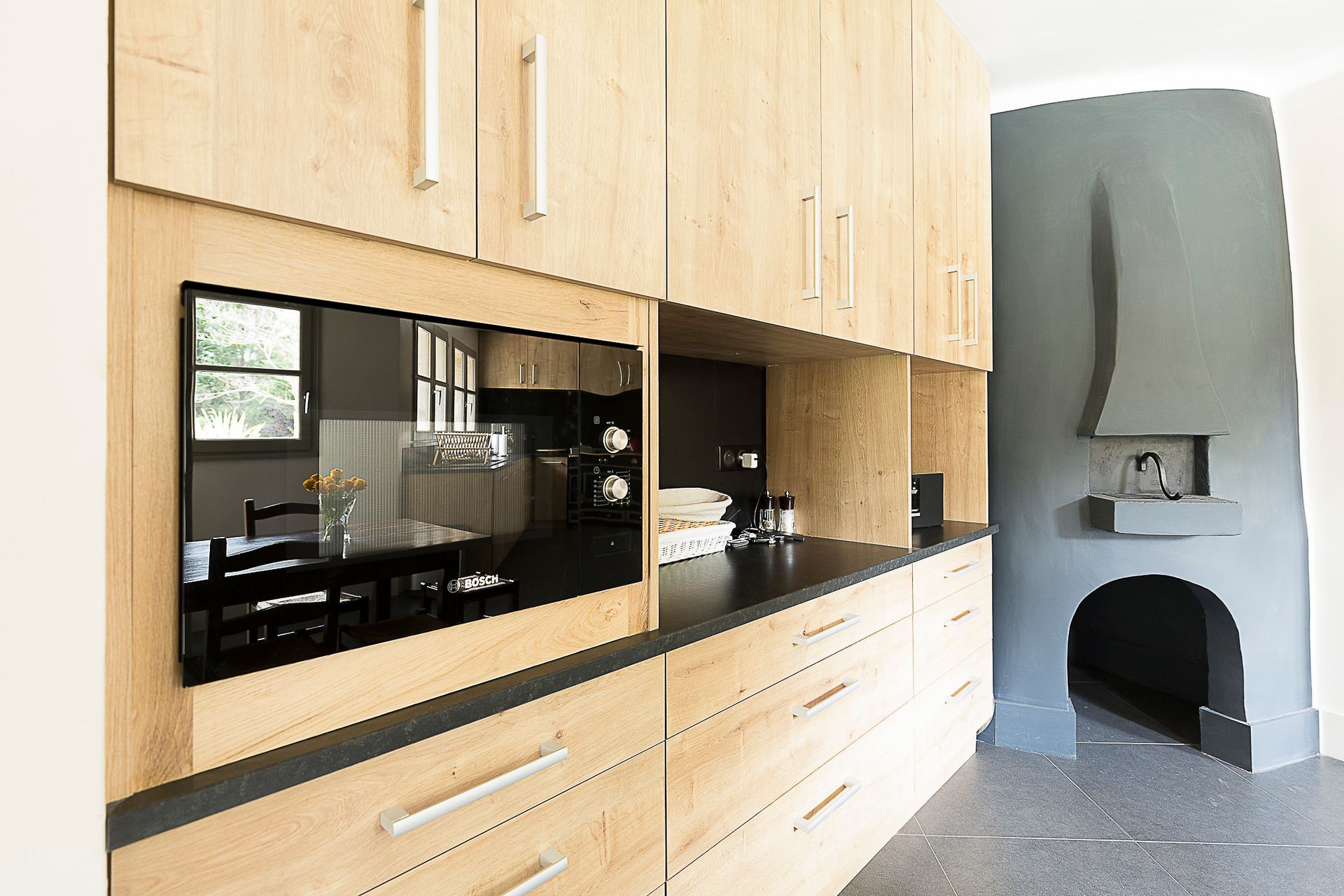 Une cuisine avec des armoires en bois, des comptoirs noirs, un four à micro-ondes et une cheminée.