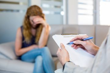 Una mujer está sentada en un sofá mientras un médico escribe en un portapapeles.